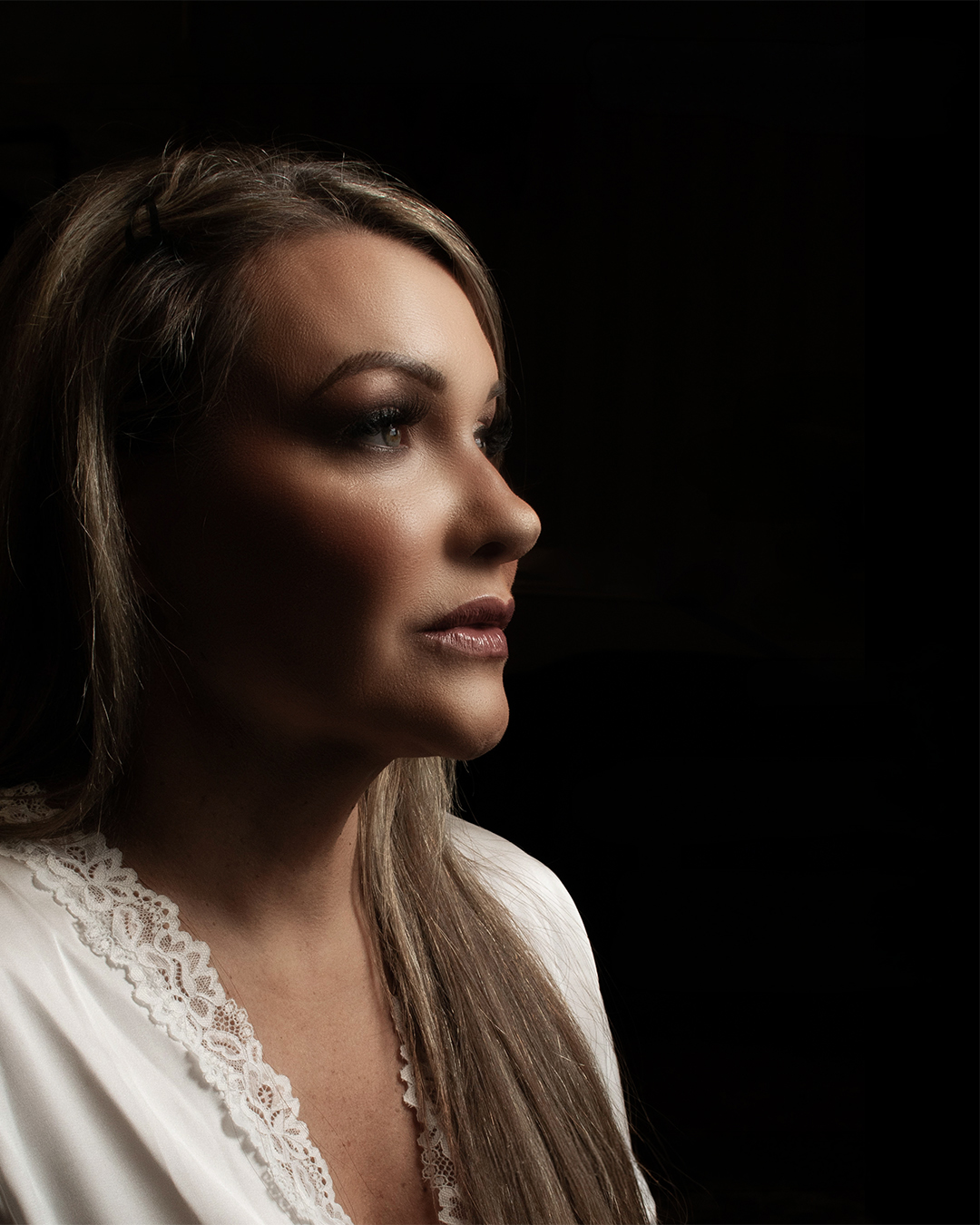 Woman in a white satin robe photographed in profile with soft light against a dark background.